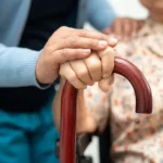 Caregiver's hand supporting a senior holding a walking cane