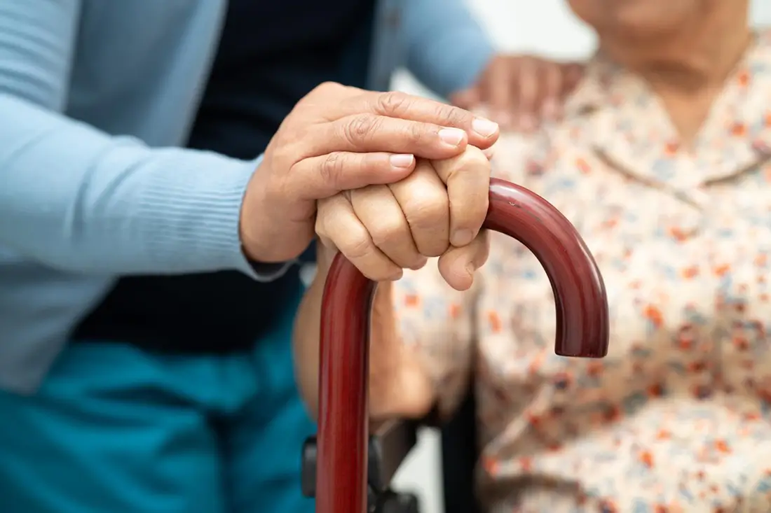 Caregiver's hand supporting a senior holding a walking cane